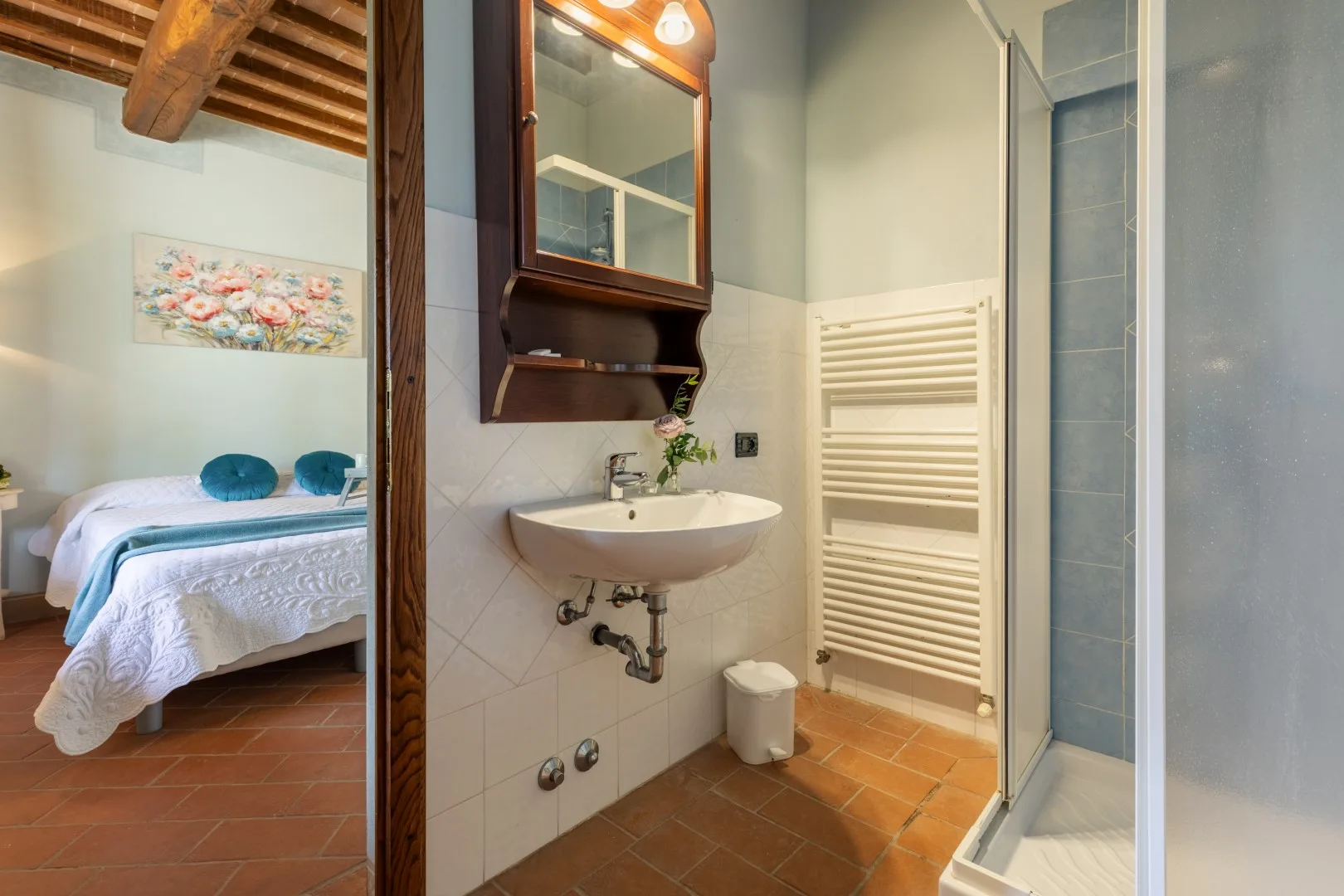 A bathroom with a wall-mounted sink and glass shower beside a bedroom.