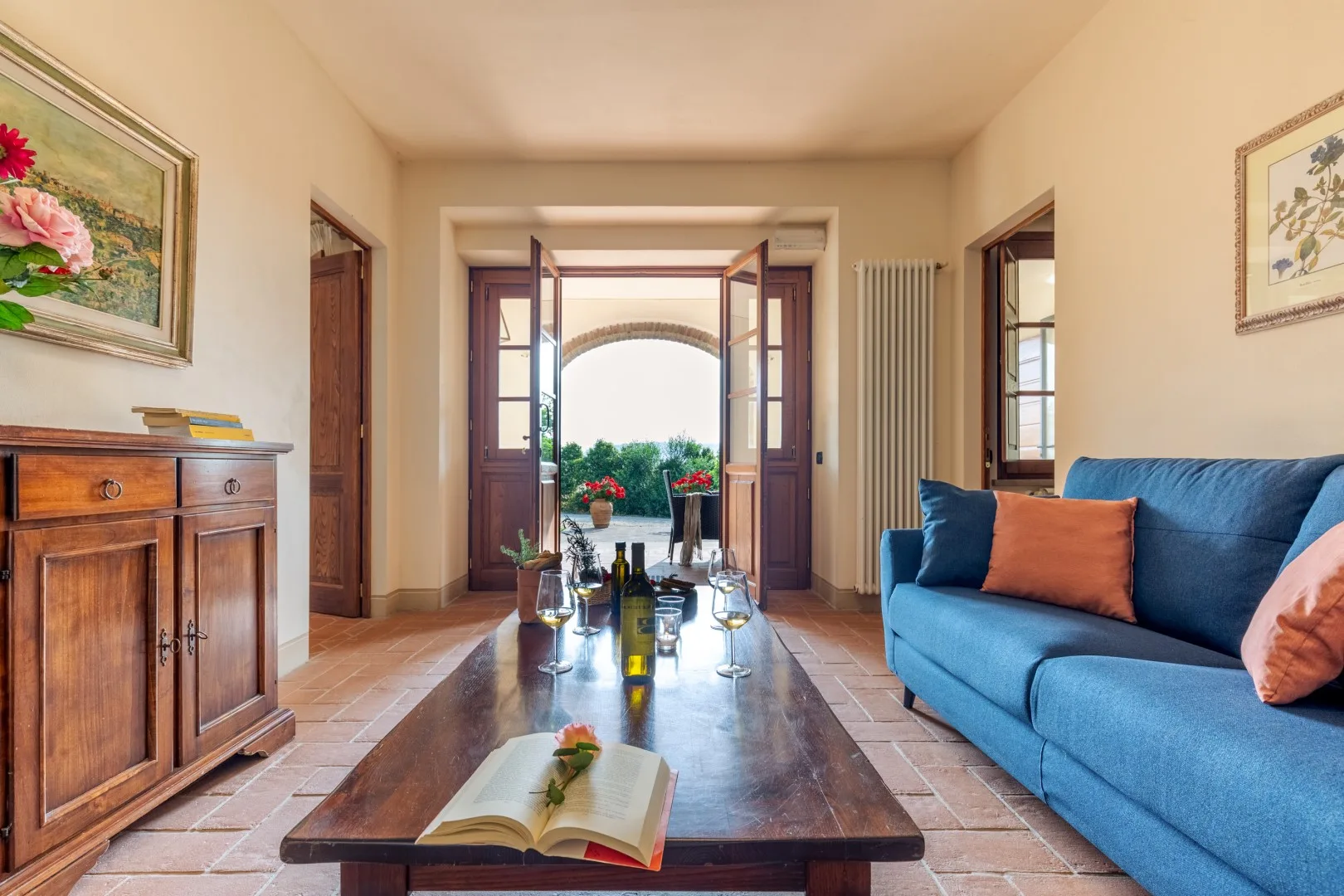 A living room with blue seating and open doors leading to a bright outdoor area.