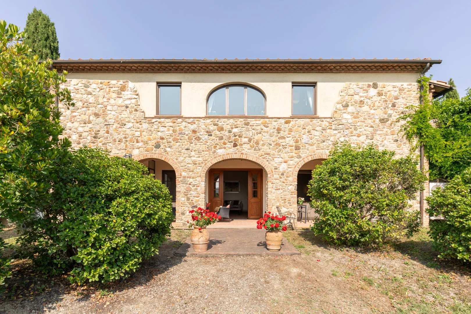 A stone building with arched entrances stands behind green shrubs.