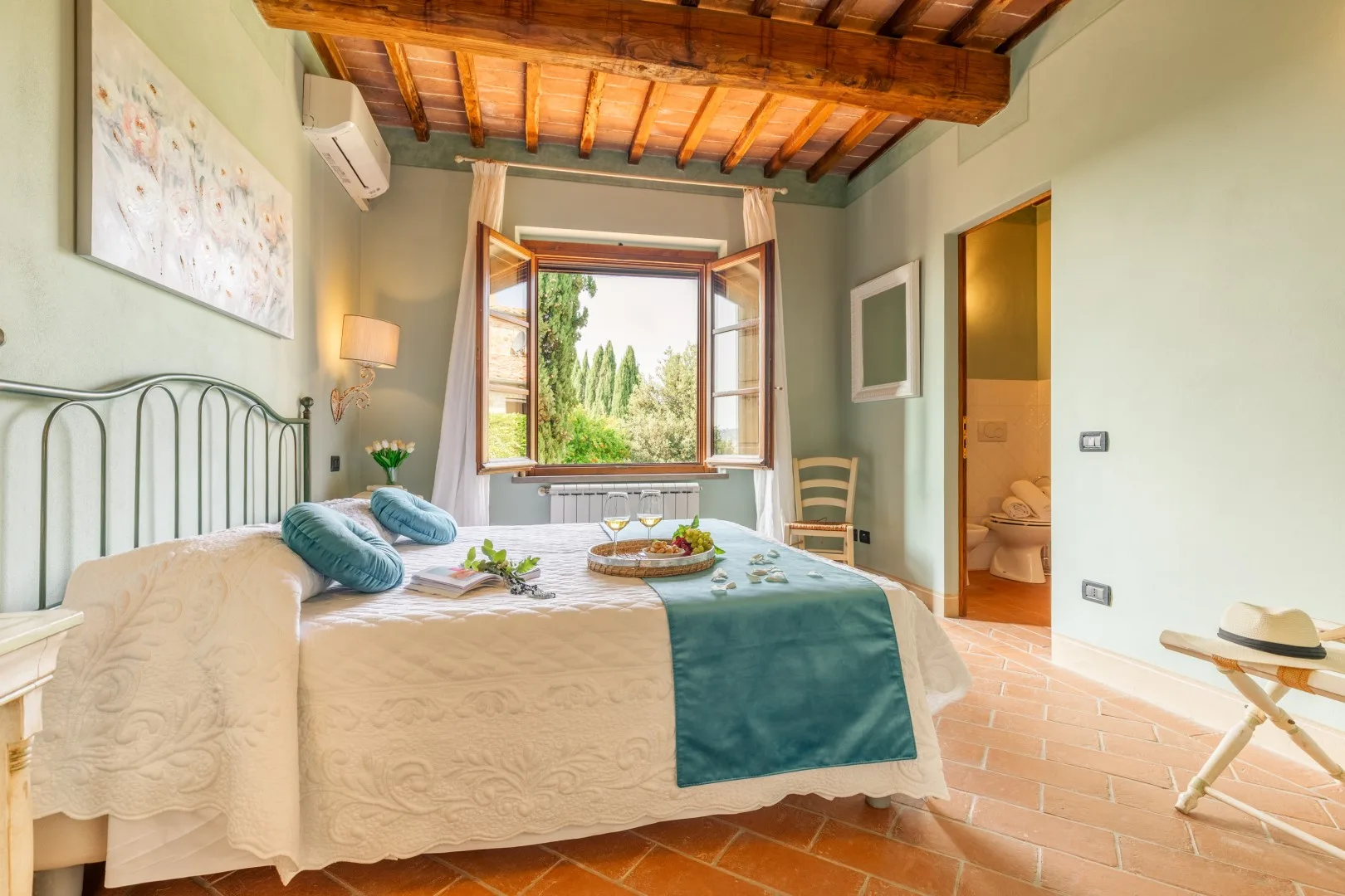 A bedroom with a double bed, an open window, and exposed wooden ceiling beams.