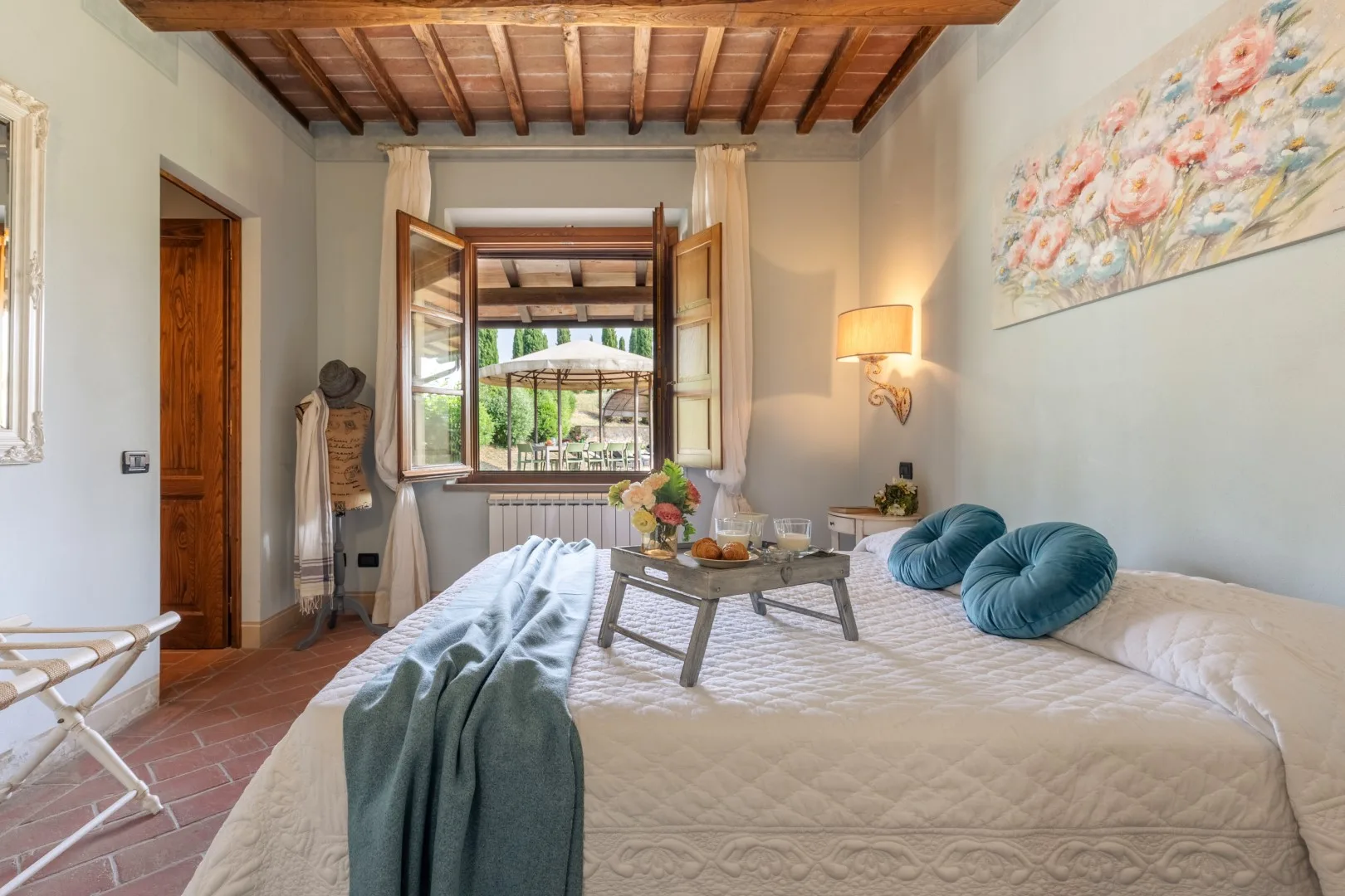 A bedroom with a large bed, bedside lamp, and open window overlooking greenery.