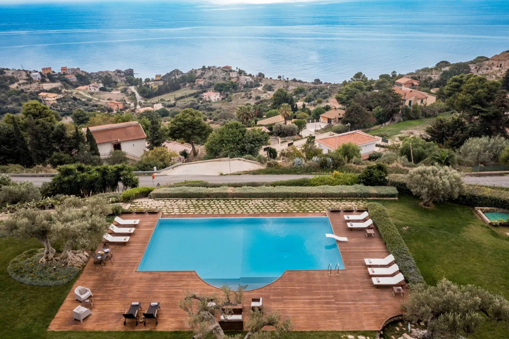Una piscina y una terraza de madera tienen vistas a una ladera costera y al mar.