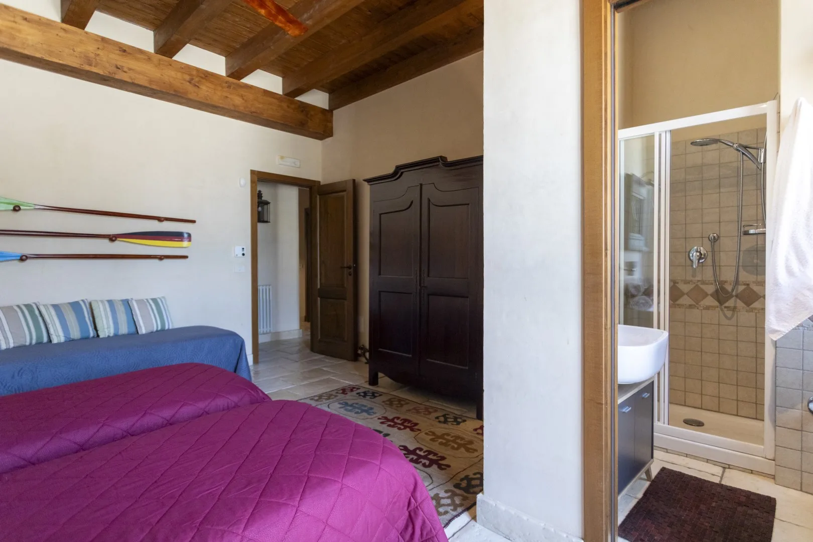 Un dormitorio con ropa de cama colorida, un armario oscuro y una ducha contigua con azulejos.