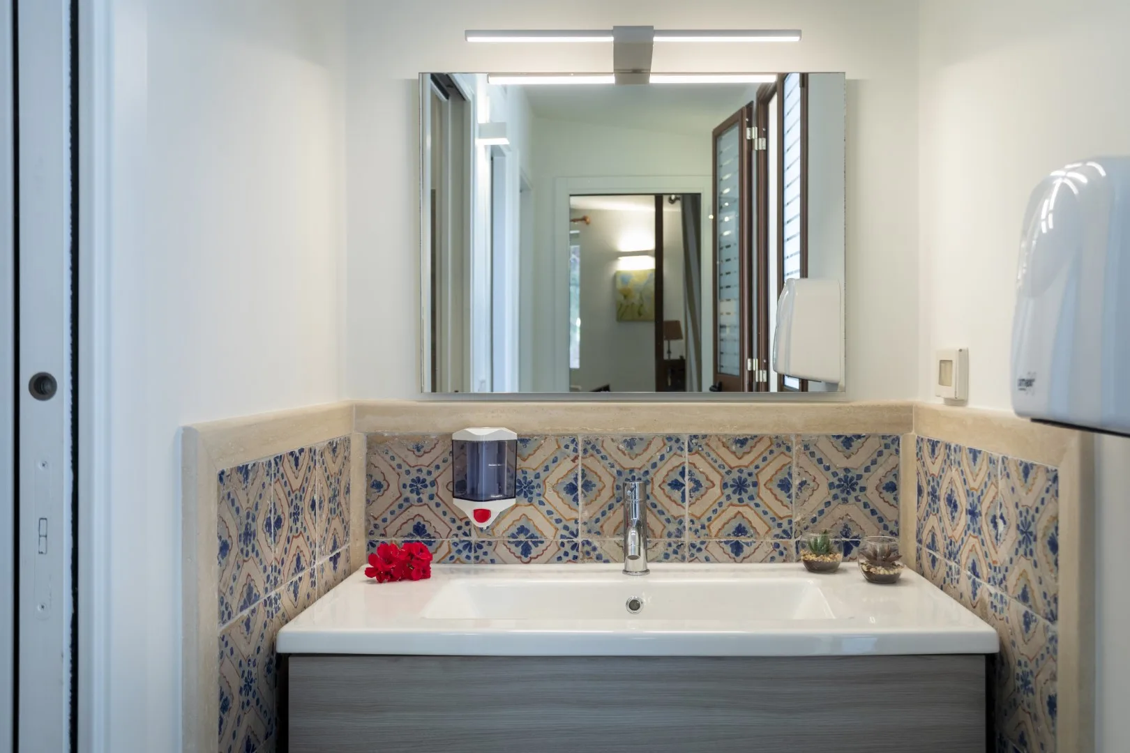 Un lavabo de baño está bajo un espejo grande y azulejos estampados.