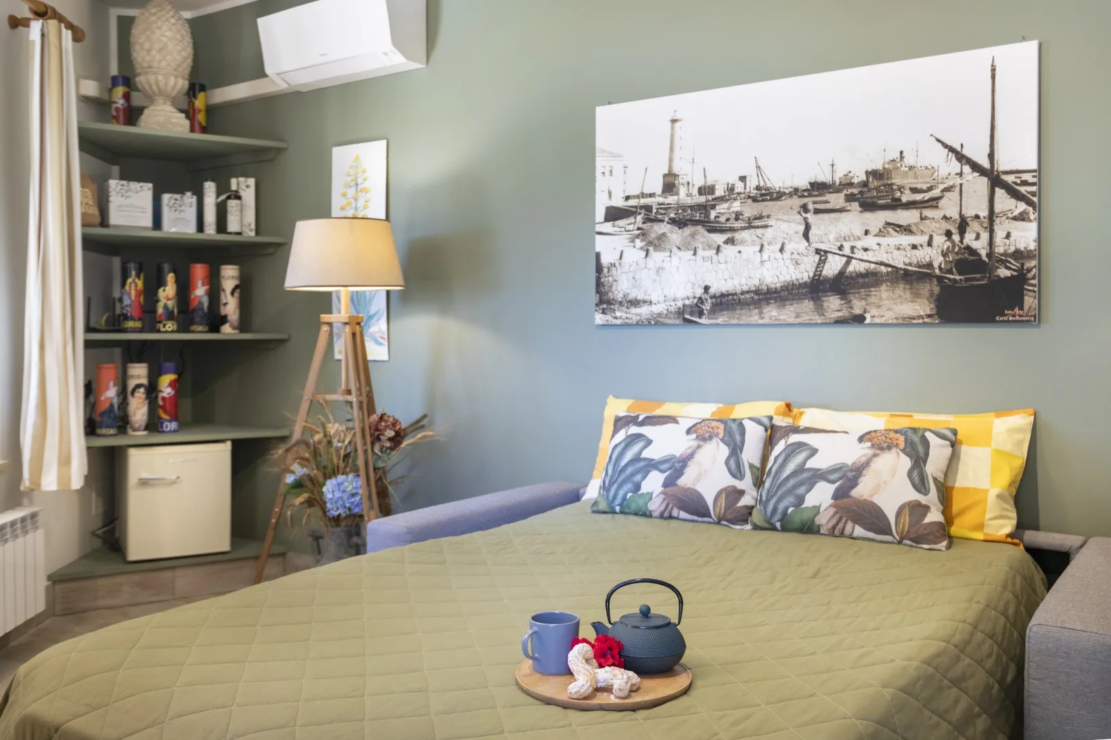 Un dormitorio con una cama, almohadas estampadas y una imagen enmarcada de un puerto en la pared.