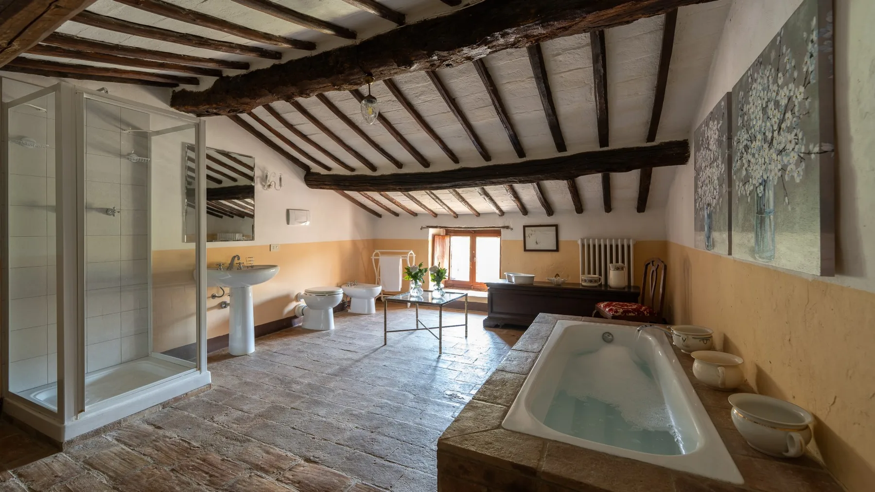 A rustic bathroom with a bathtub, glass shower, and exposed ceiling beams.