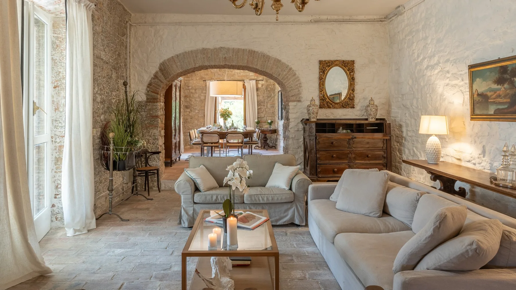 A living room with pale seating and a stone archway opening onto a dining area.