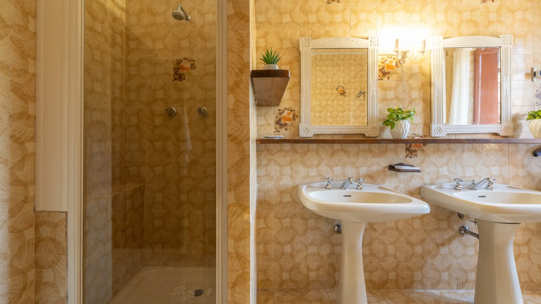 A tiled bathroom with a glass shower and two pedestal sinks.