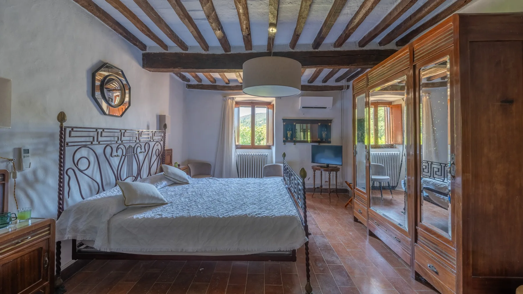 A bedroom with a large bed, exposed ceiling beams, and a wooden wardrobe.