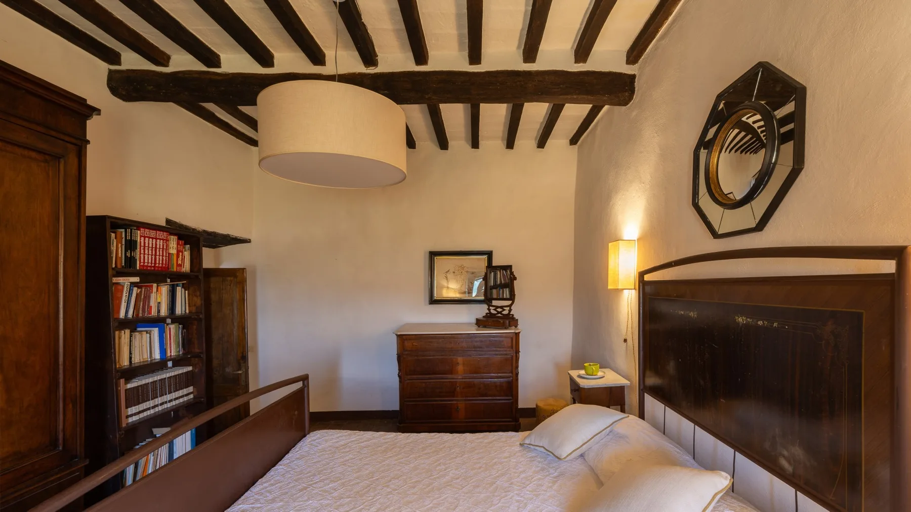 A bedroom with a bed, wooden furnishings, and exposed ceiling beams.