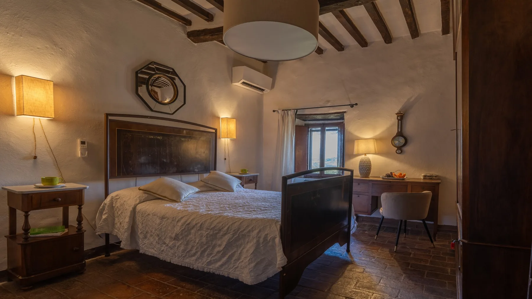 A bedroom with a large bed and a desk beside the window.