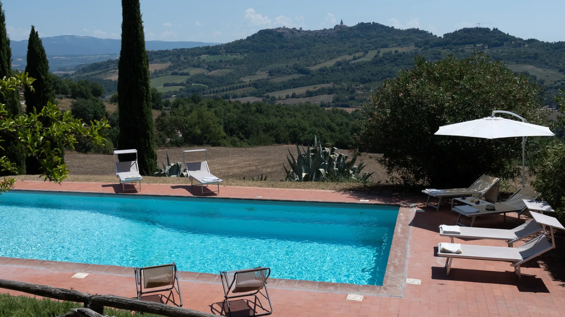 An outdoor swimming pool overlooks green hills and a rural landscape.