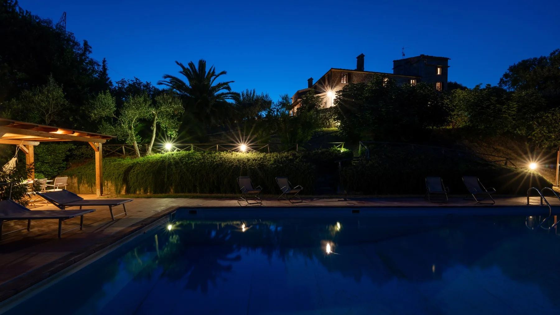 An outdoor swimming pool at dusk, with loungers and garden lighting.