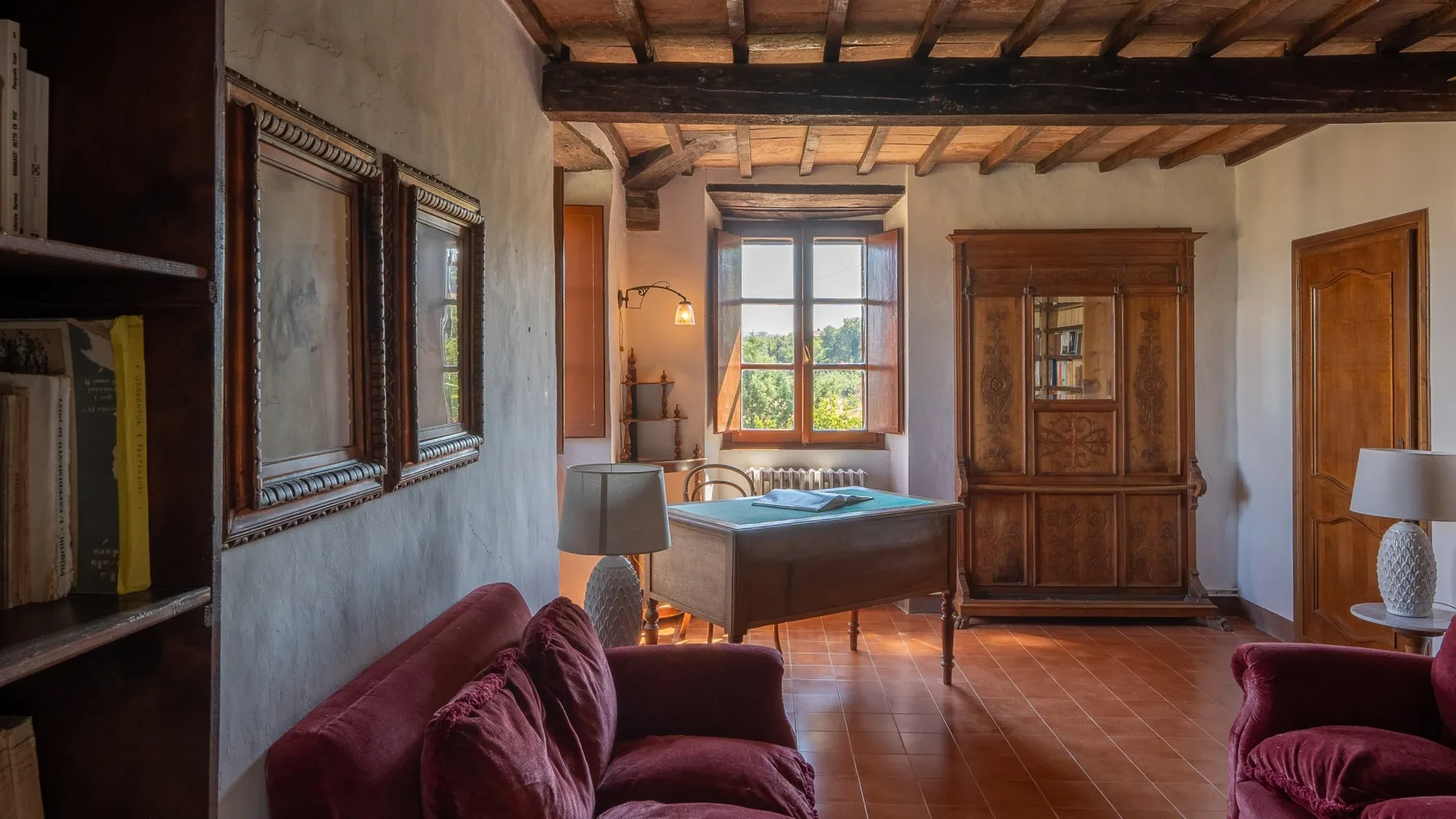 A rustic living room with burgundy seating, a desk, and a wooden cabinet.