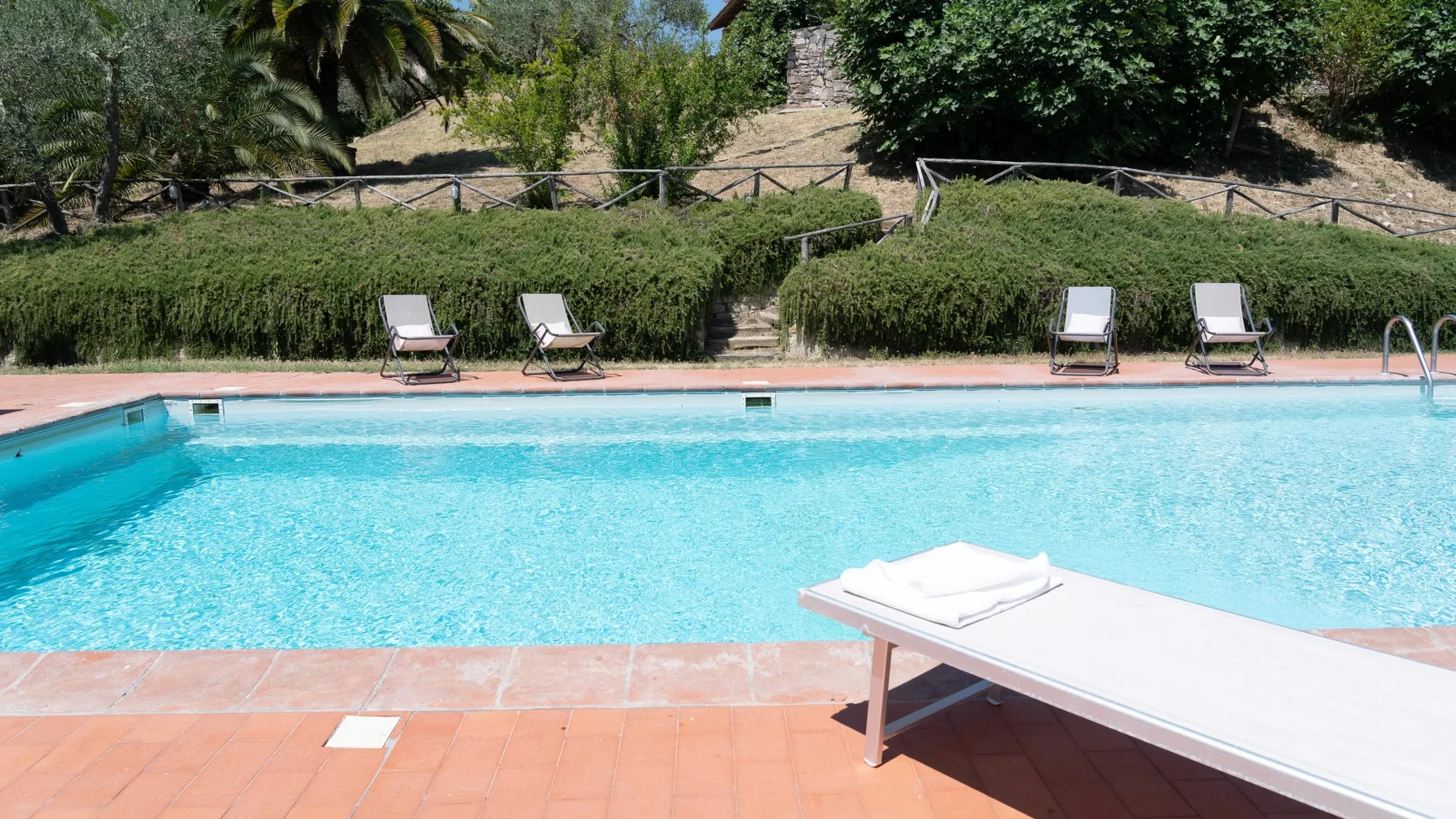 An outdoor swimming pool bordered by terracotta-colored paving and greenery.
