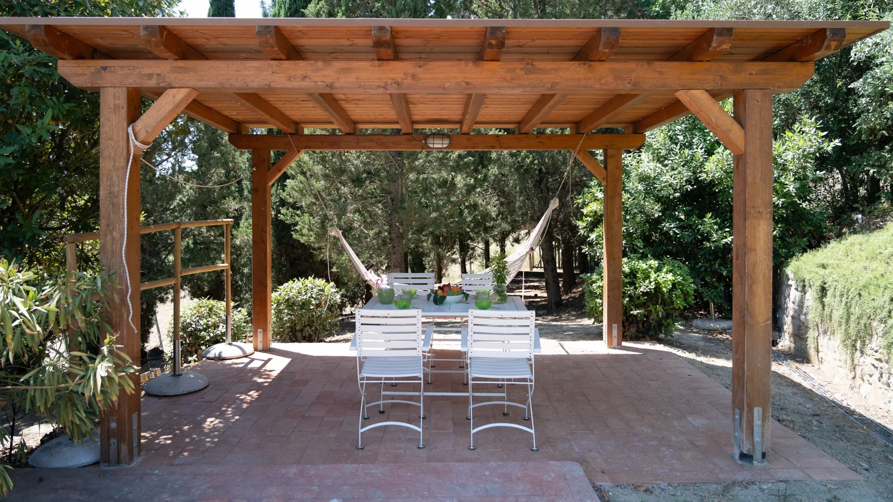 A shaded outdoor dining area sits beneath a wooden pergola, with a table and chairs.