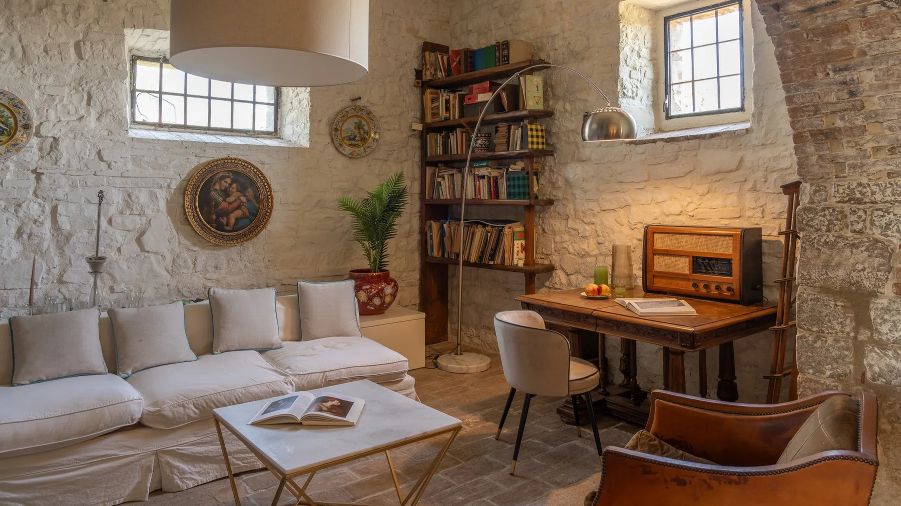 A rustic living room with pale seating, a wooden desk, and bookshelves.