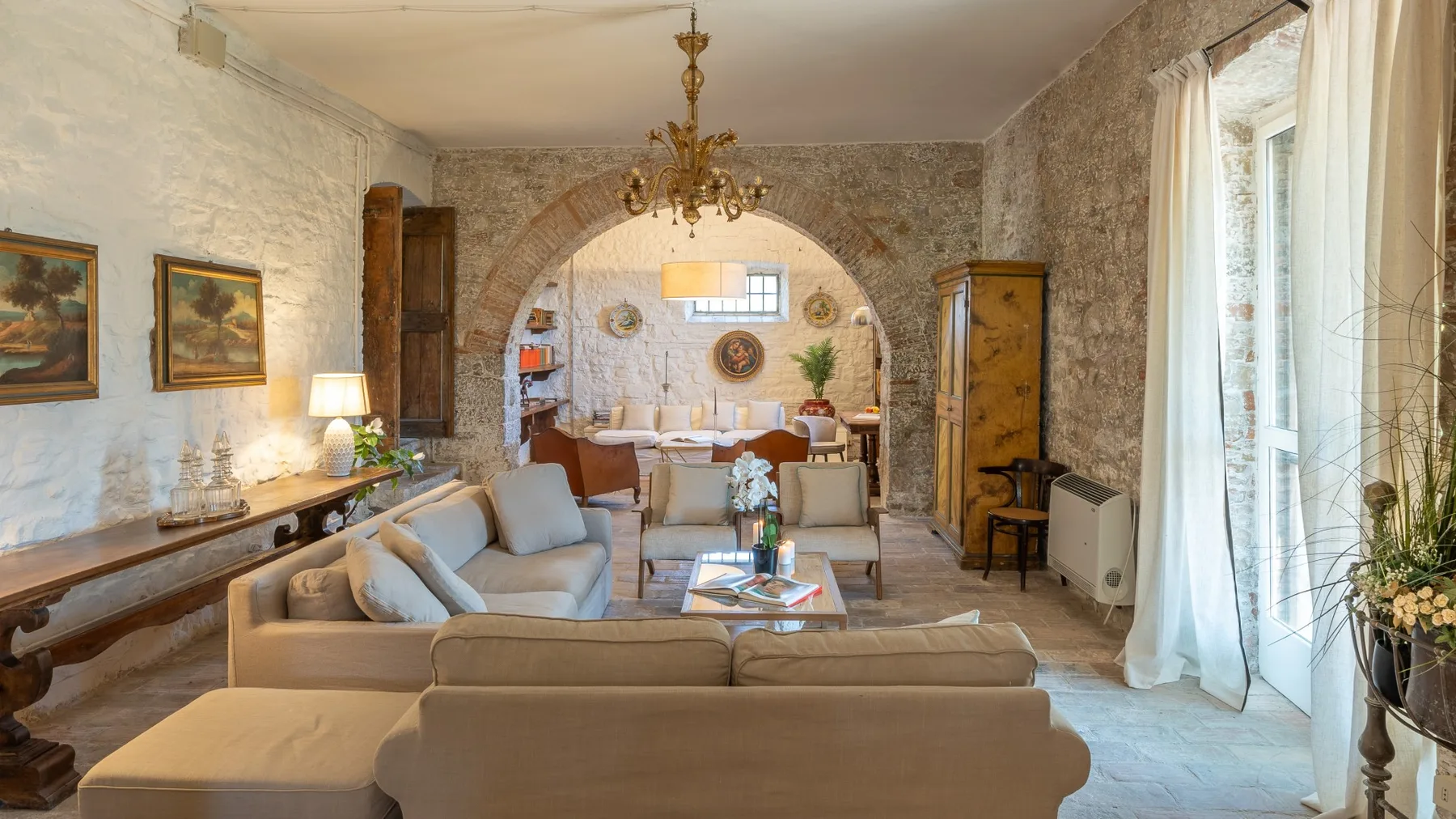 A living room with seating arranged around a low table beneath a stone arch.