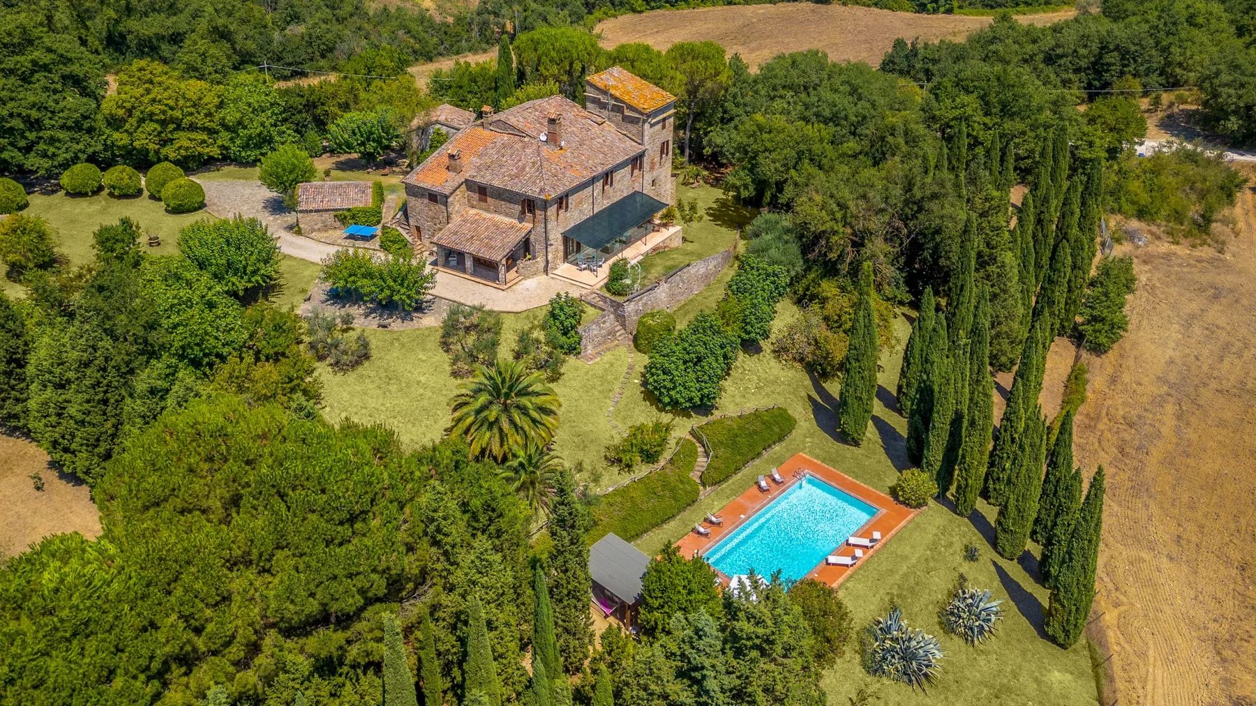 Aerial view of a countryside house and swimming pool surrounded by greenery.