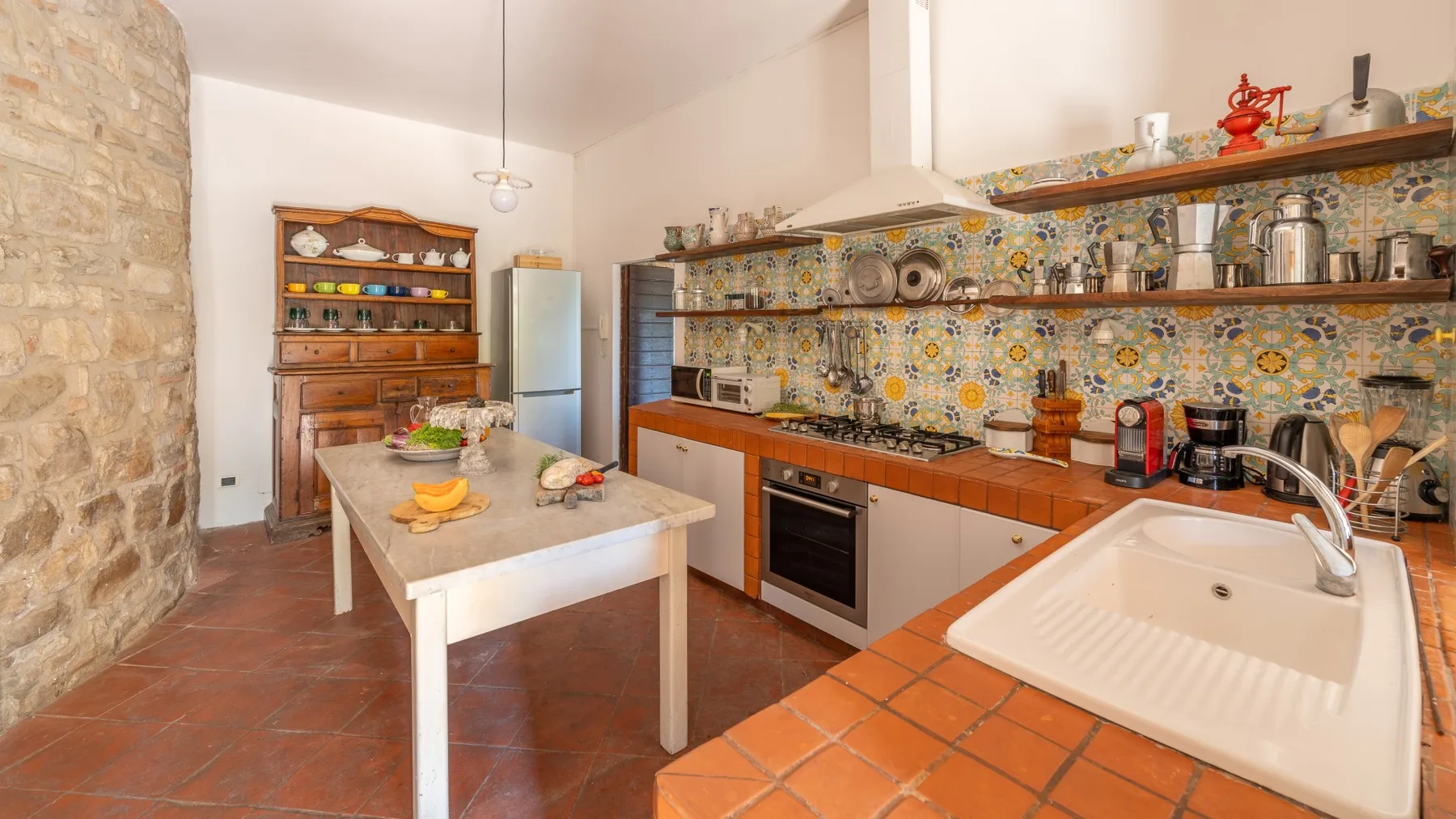 A spacious kitchen with a tiled backsplash, wooden cabinets, and a central table.