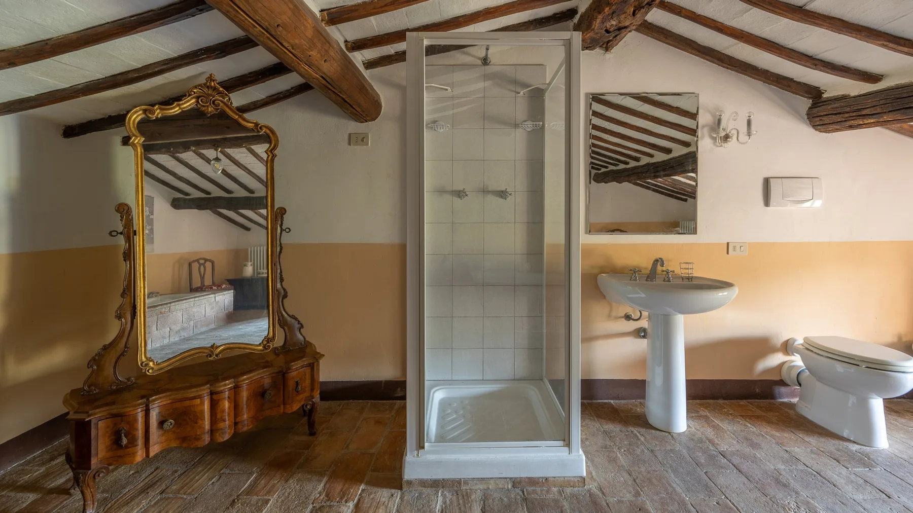 A rustic bathroom with a glass shower, sink, toilet, and ornate mirror.