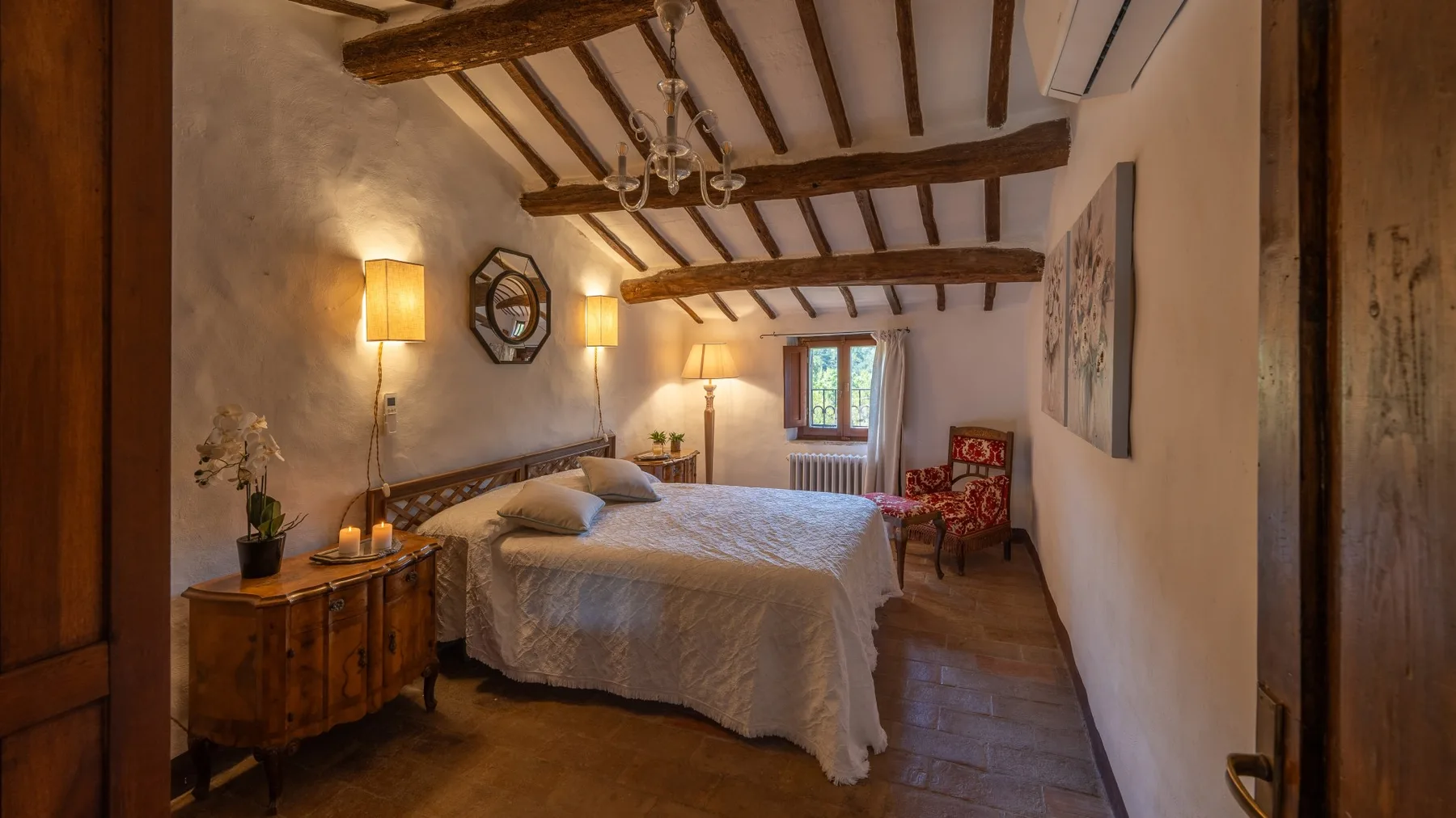 A bedroom with a bed, wooden beams, and a window at the far end.