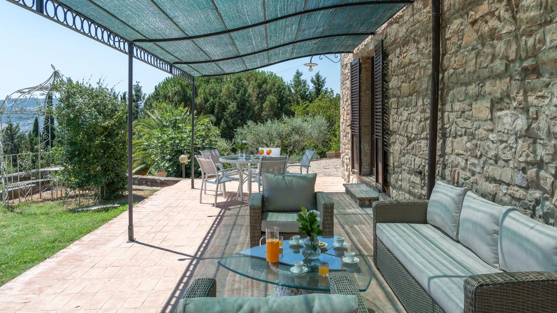 A shaded outdoor patio with seating and a glass-topped table.