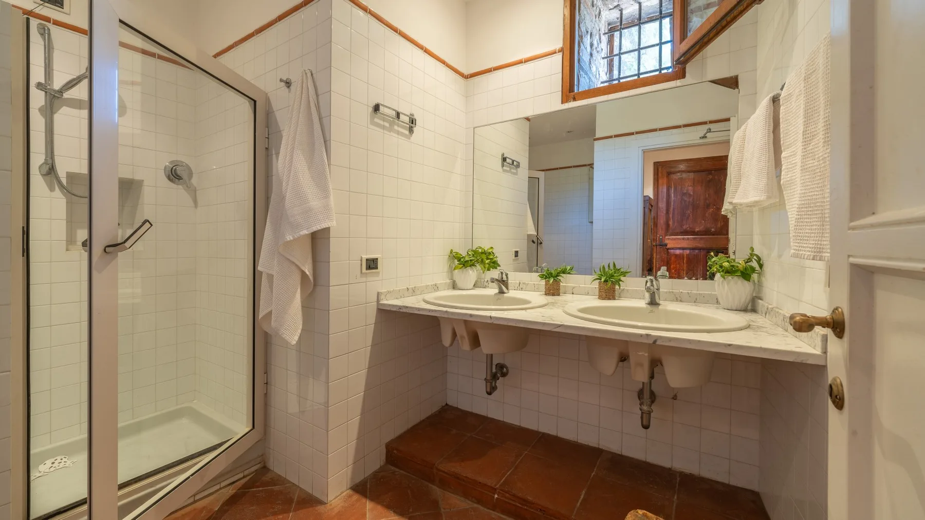 A tiled bathroom with a glass shower and a double sink vanity.