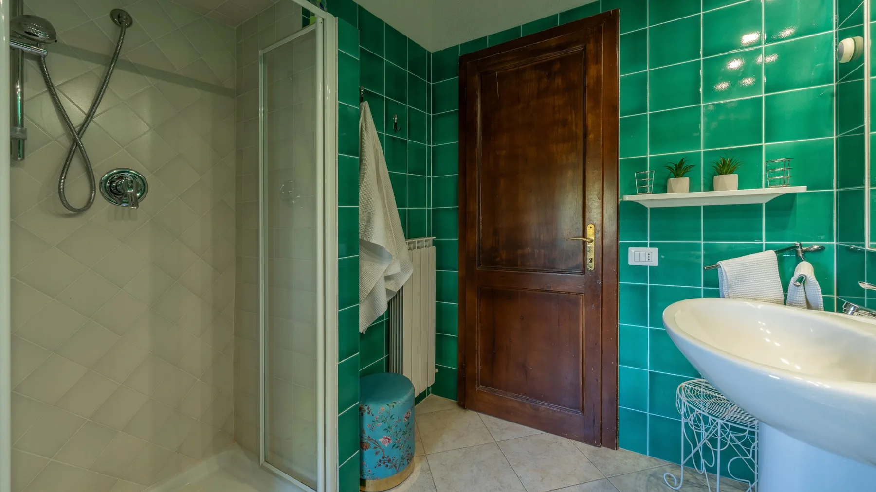 A tiled bathroom with a glass shower, wooden door, and white sink.