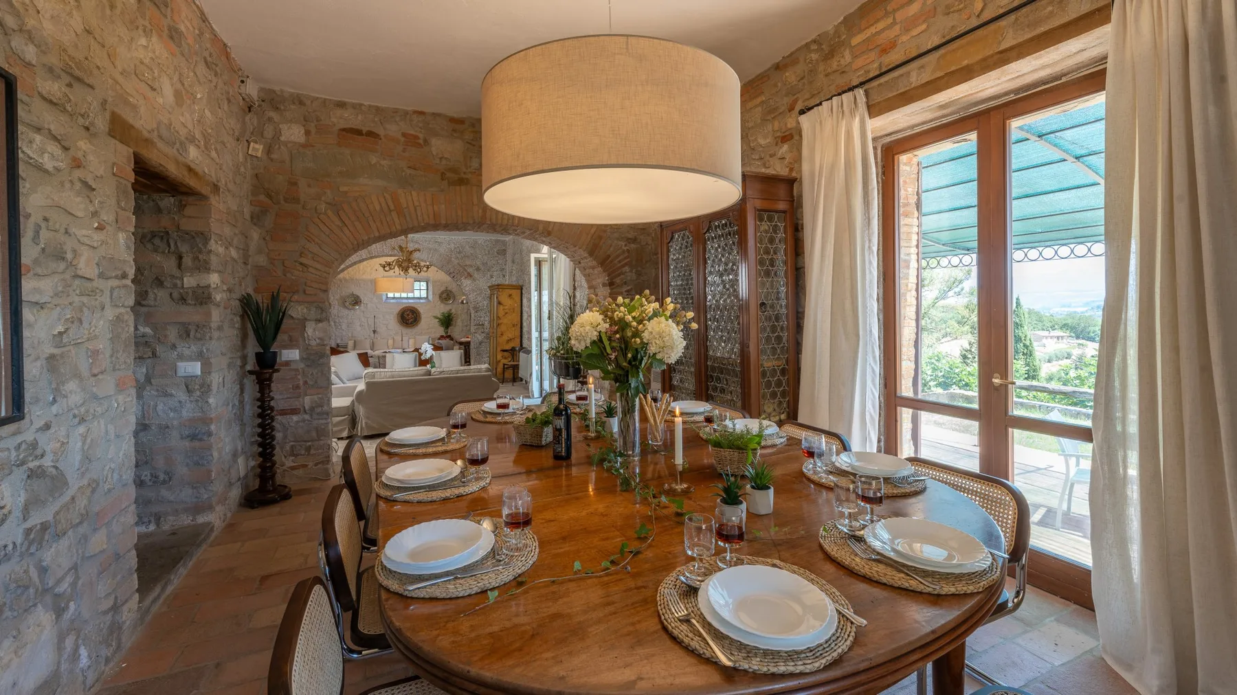 A dining room with a long wooden table set beside large windows.