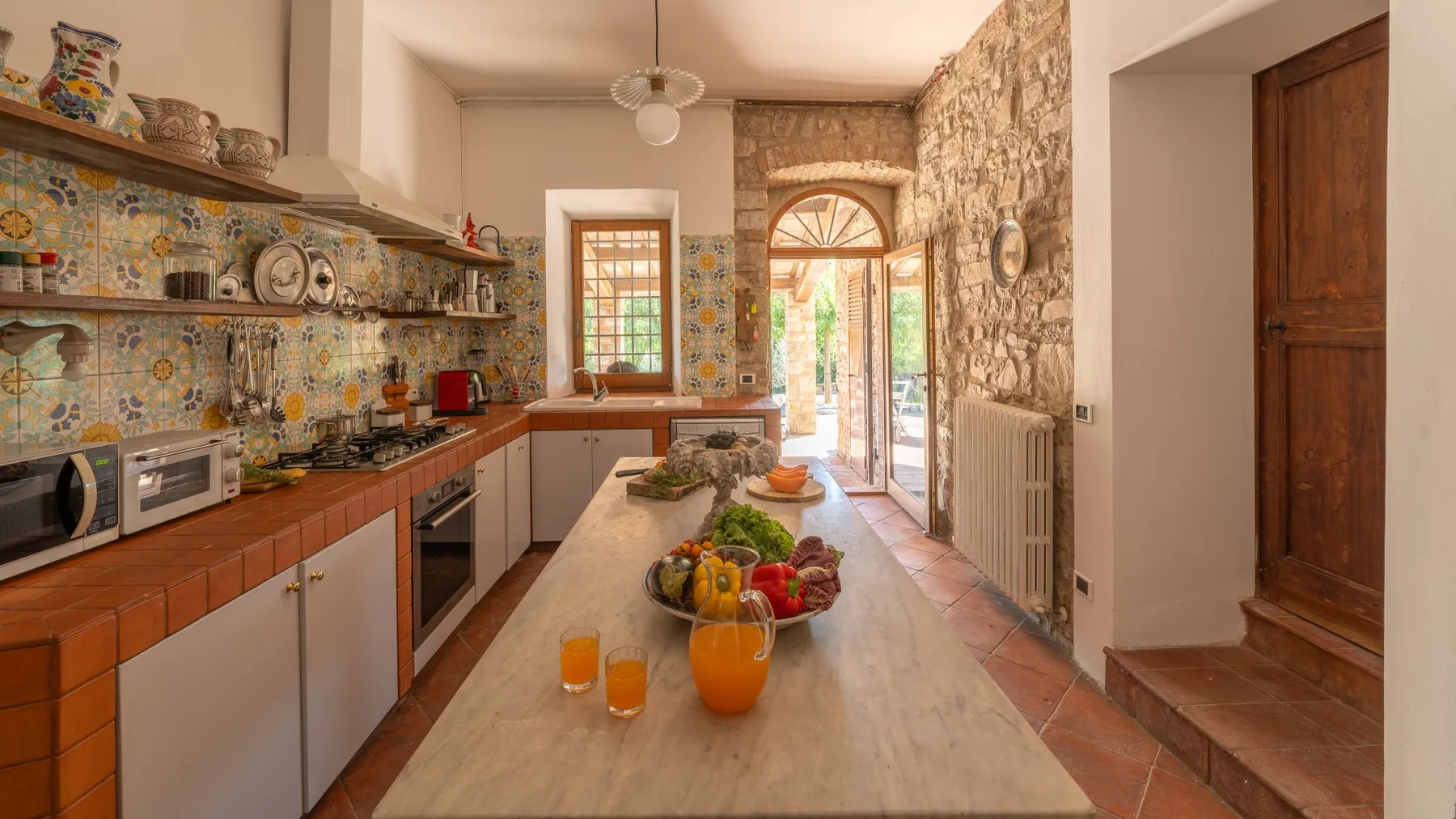 A rustic kitchen with a long central counter and colorful patterned tiles.