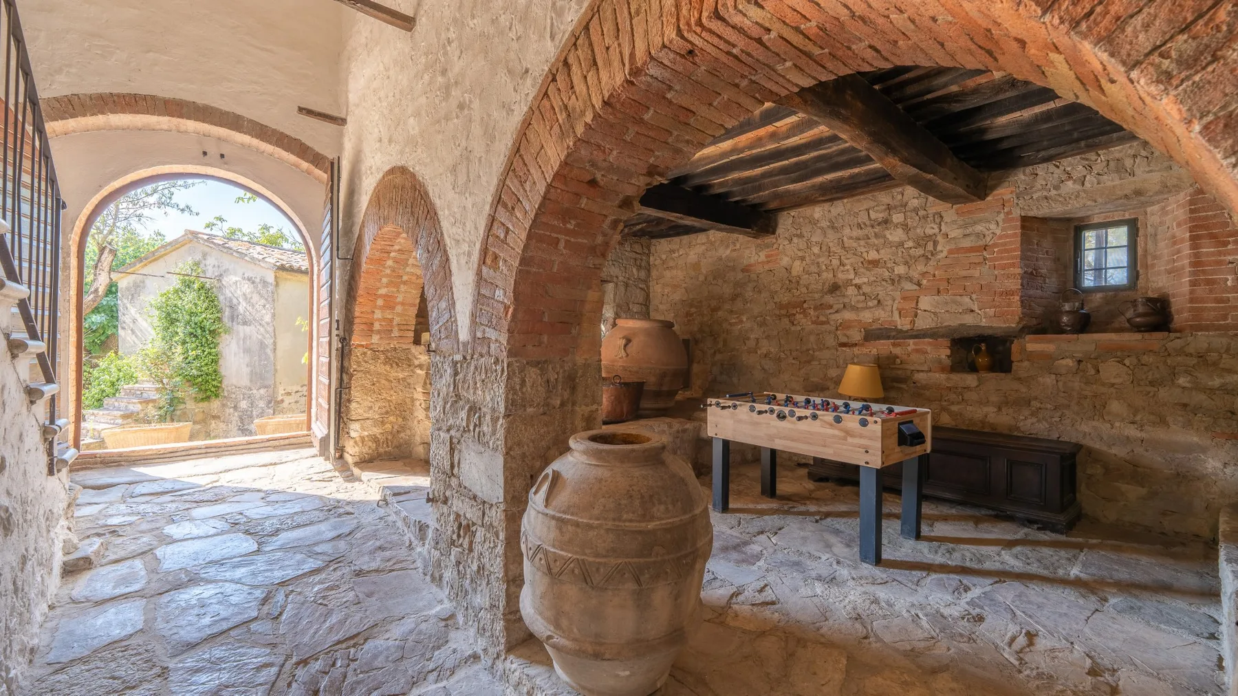 A rustic stone room with brick arches, a foosball table, and large pottery.