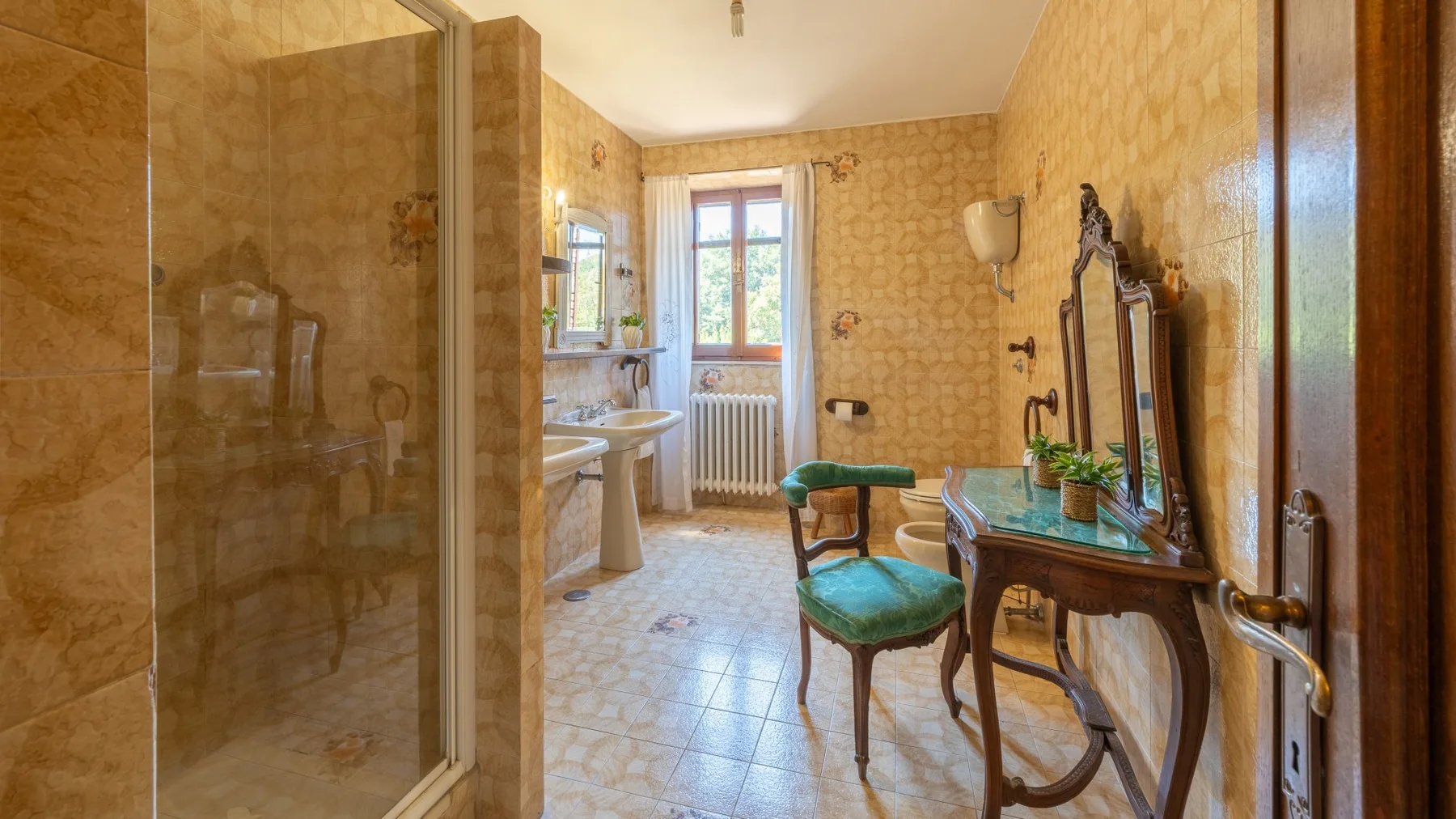 A tiled bathroom with a glass shower, a sink, and a chair.