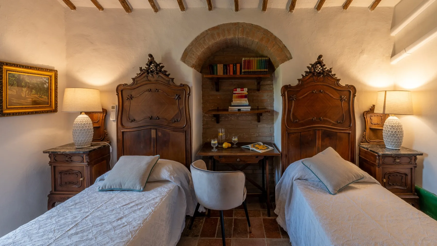 A bedroom with two beds and a small table beneath an arched bookshelf.