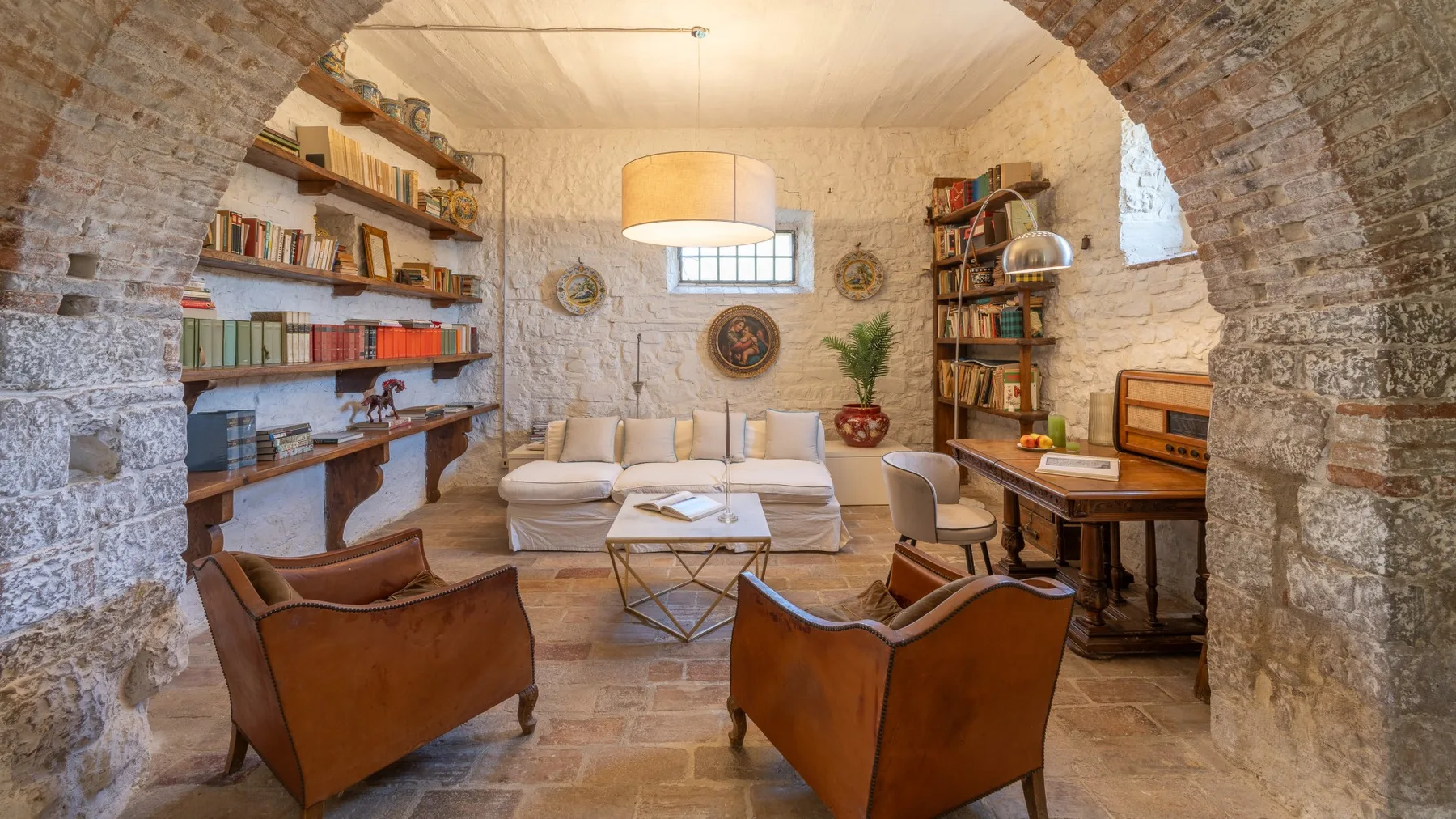 A living room with seating, bookshelves, and a coffee table beneath a stone arch.