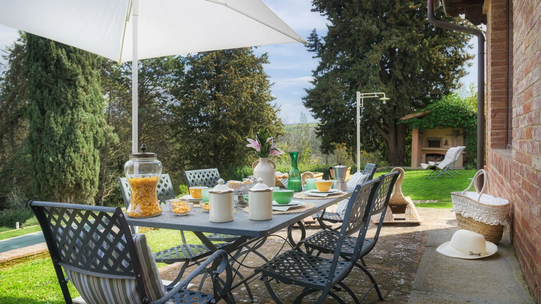 Un comedor en un patio al aire libre está bajo una gran sombrilla, frente a un jardín.