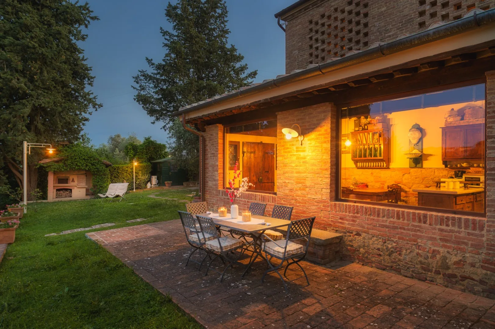 Una casa de ladrillo da a un patio ajardinado con muebles de comedor al aire libre y césped.