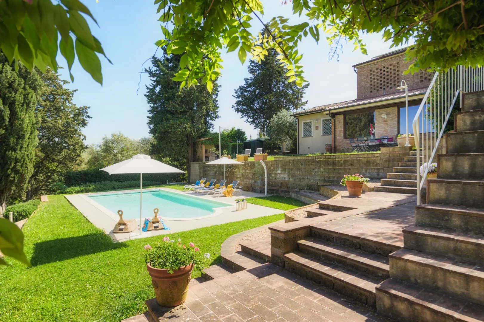Una piscina en el jardín junto a un patio elevado con escalones y asientos al aire libre.