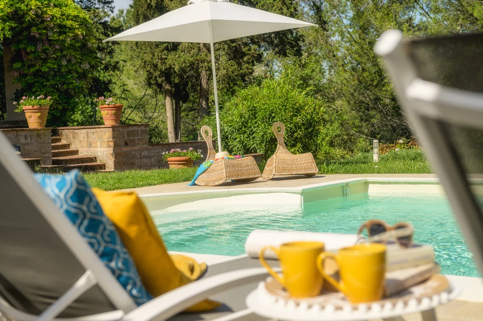 Una piscina al aire libre con una zona de descanso a la sombra y vegetación.