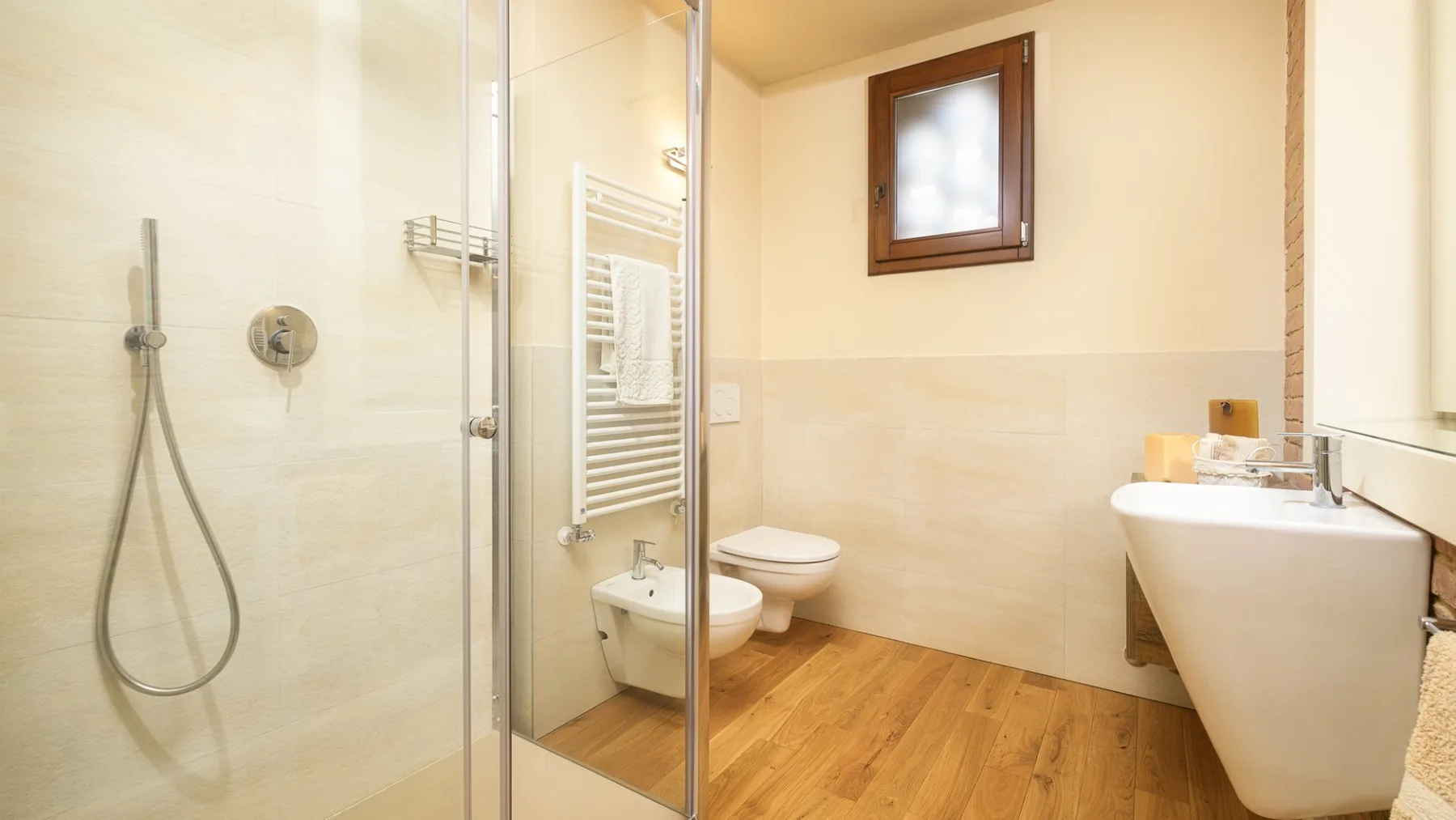 Un baño luminoso con ducha de vidrio, bañera y suelo de madera.