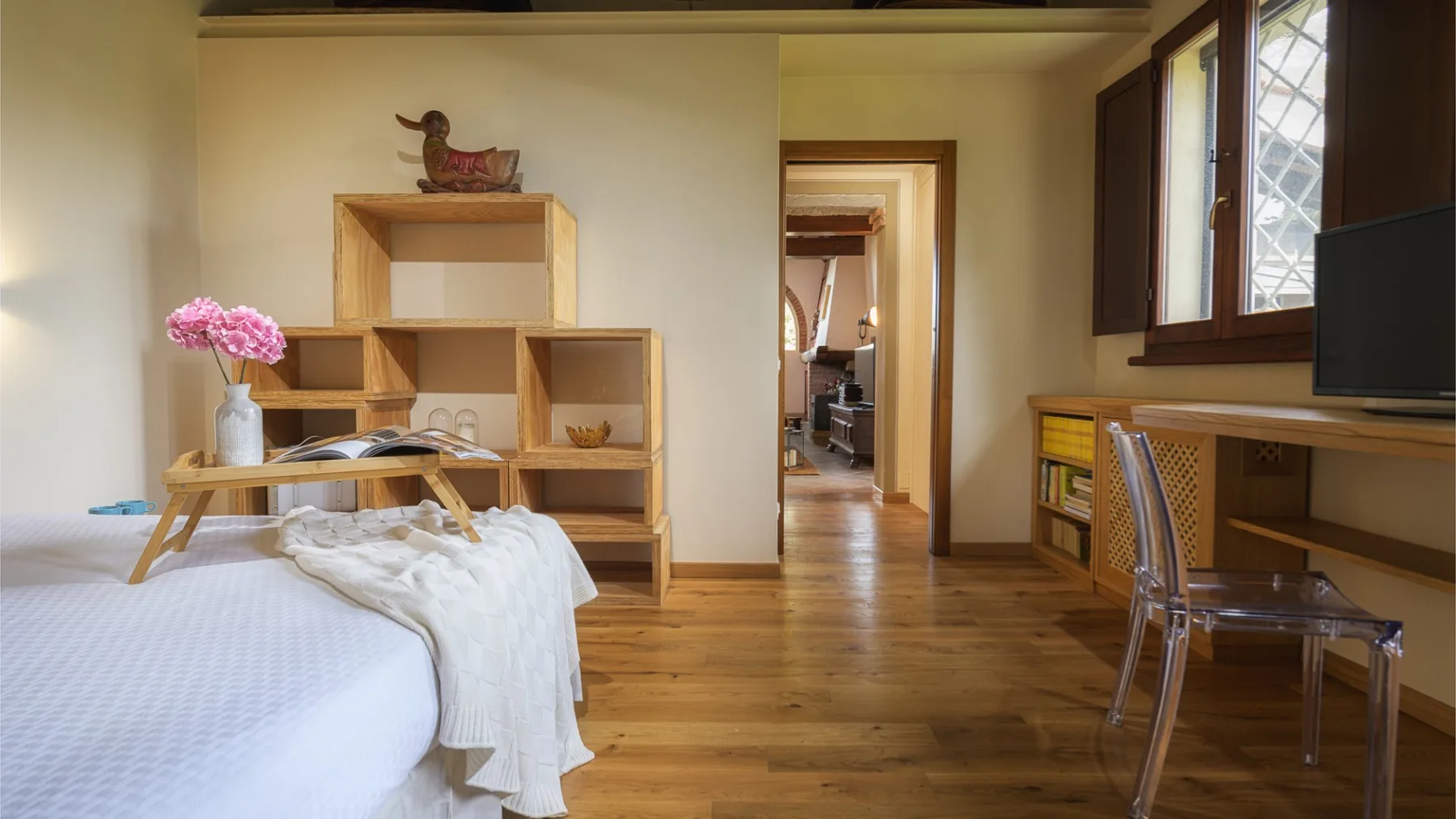 Un dormitorio con una cama, estanterías abiertas de madera y un escritorio junto a la ventana.