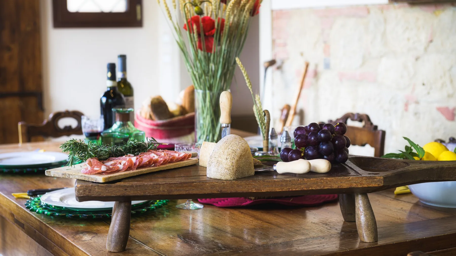 Una mesa de comedor está preparada con una tabla de madera, uvas, pan y flores.