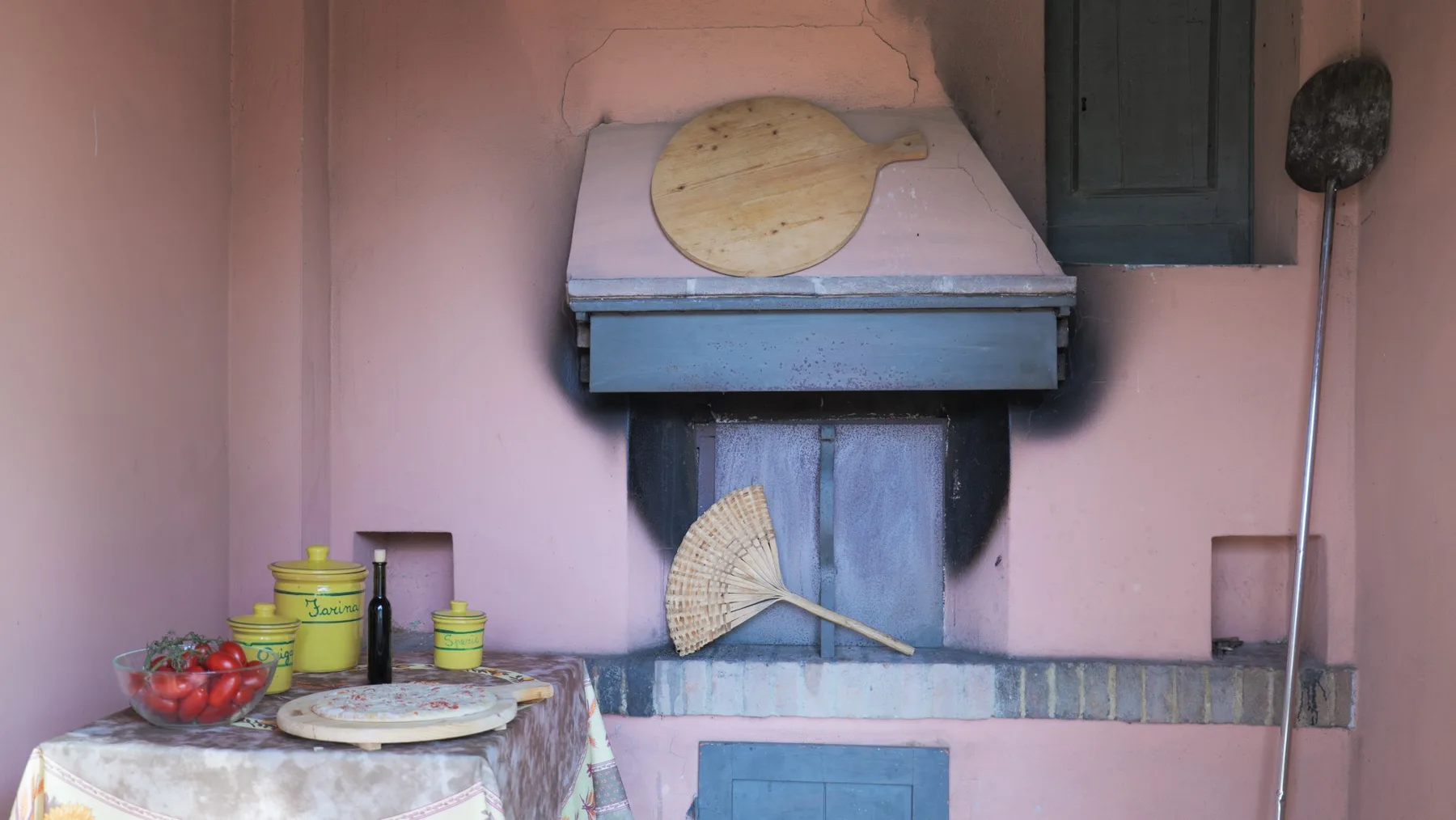 A pink-walled kitchen area with a cooking hearth and a small table of dishes.