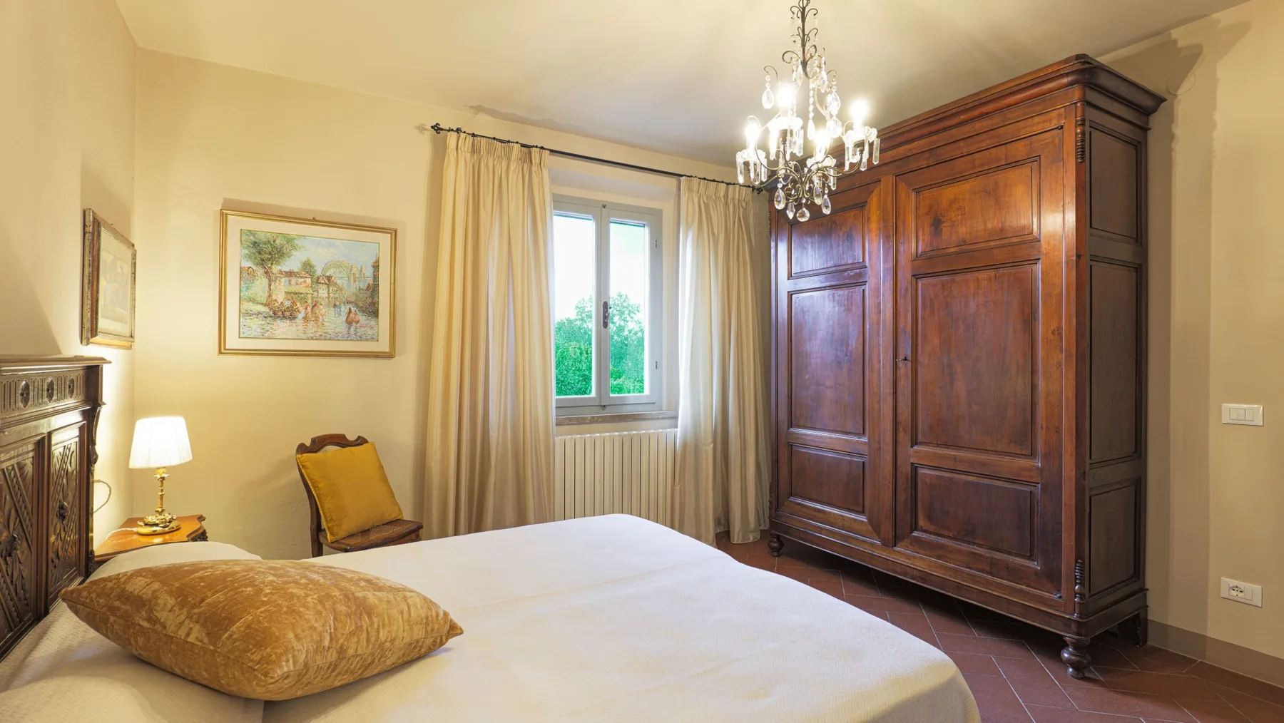 A bedroom with a bed, a window, and a large wooden wardrobe.