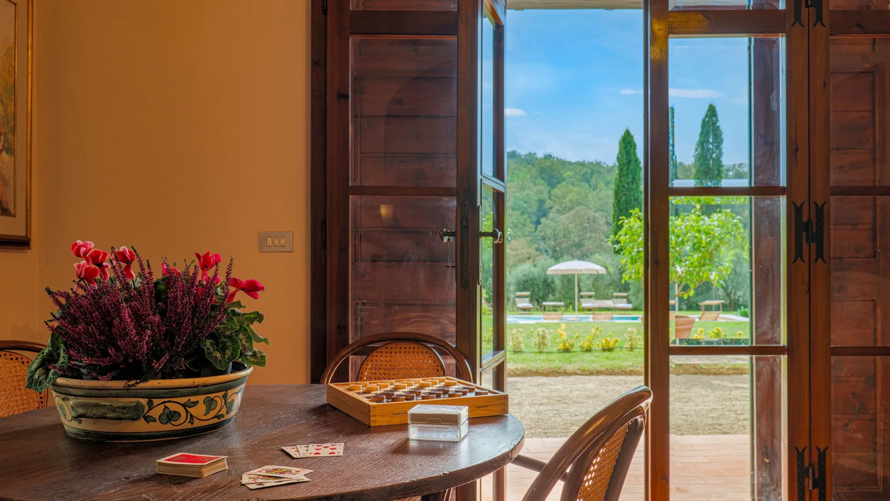 A dining area with a wooden table beside open doors overlooking a garden.