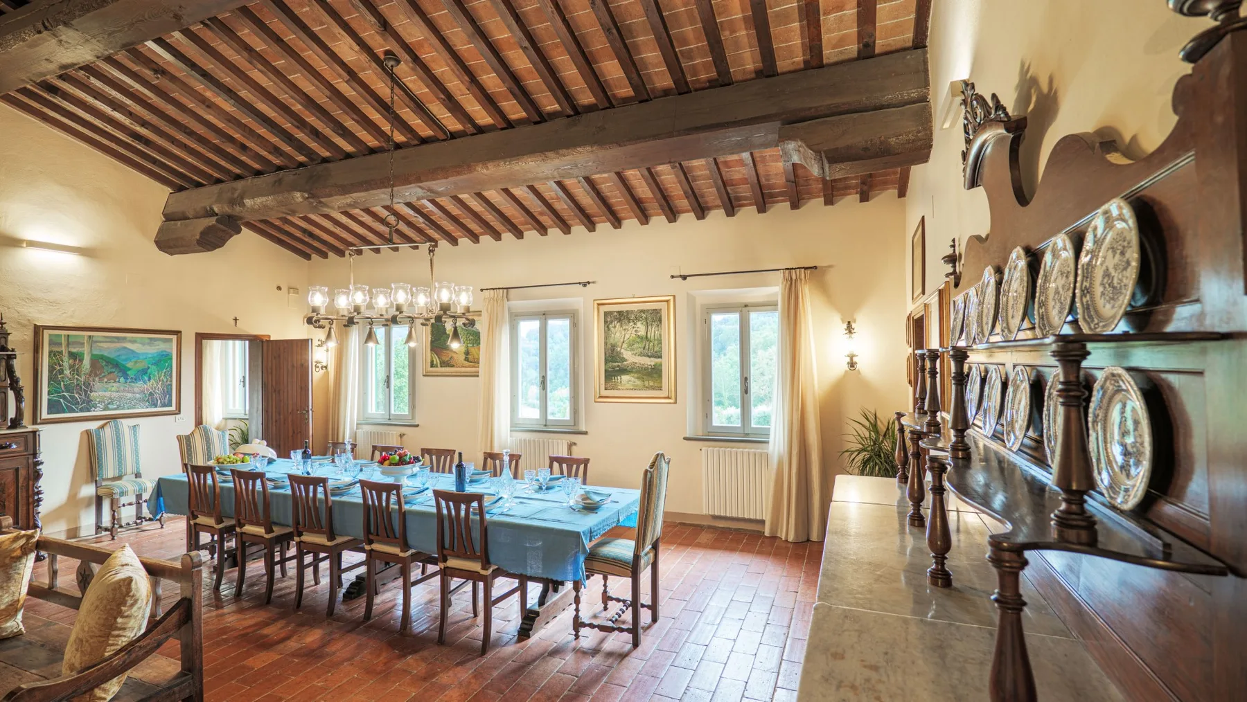 A dining room with a long table beneath exposed wooden ceiling beams.