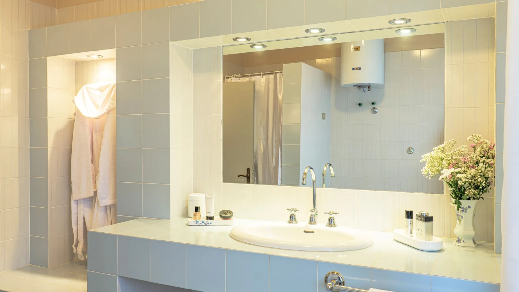 A tiled bathroom vanity with a wide mirror, sink, and flowers.