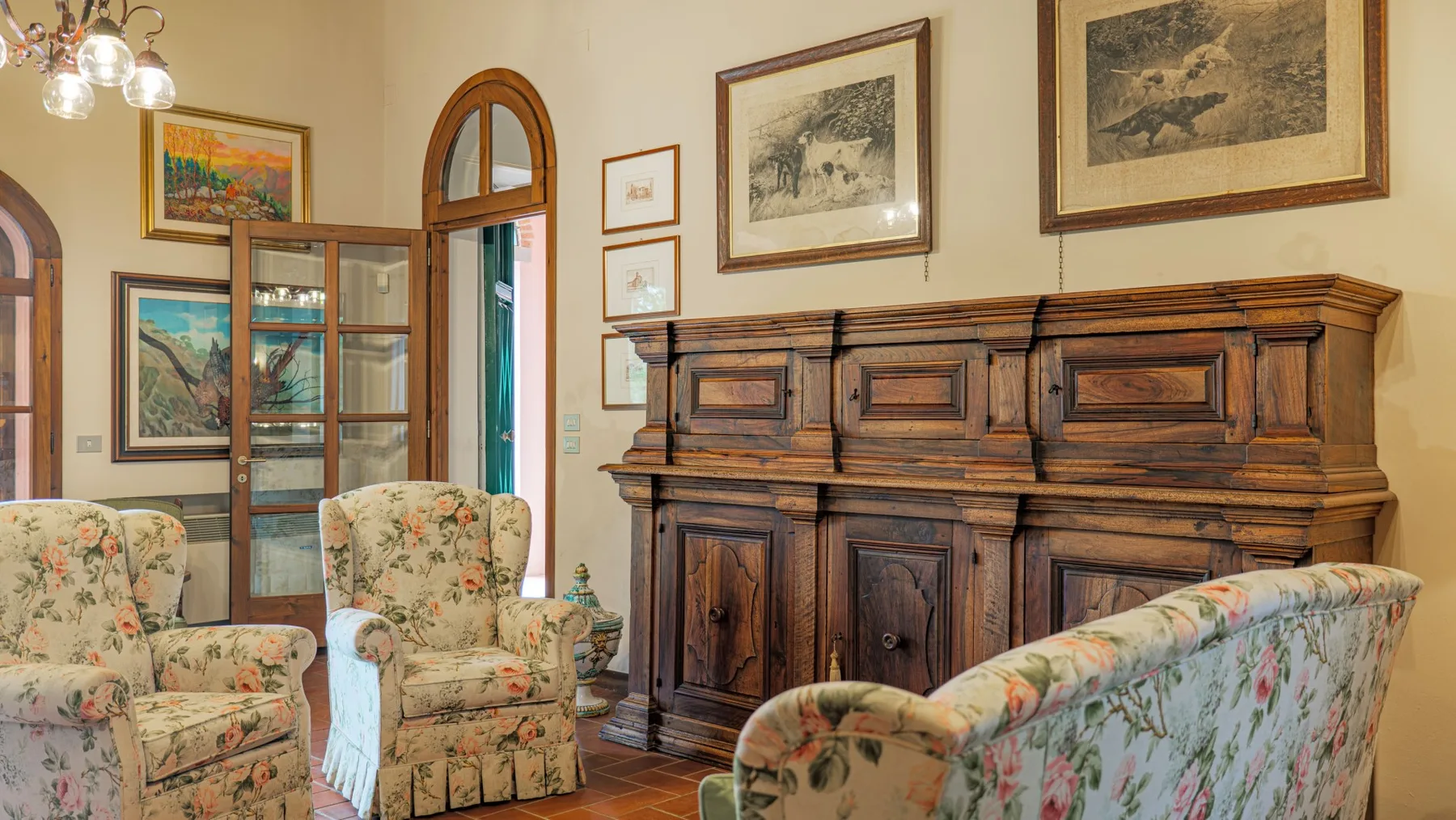 A traditional sitting room with floral seating and a large wooden cabinet.