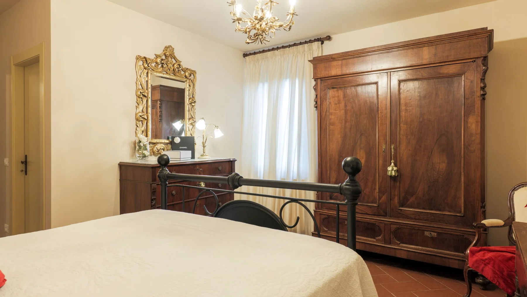 A bedroom with a bed, dark wooden furnishings, and a window with sheer curtains.
