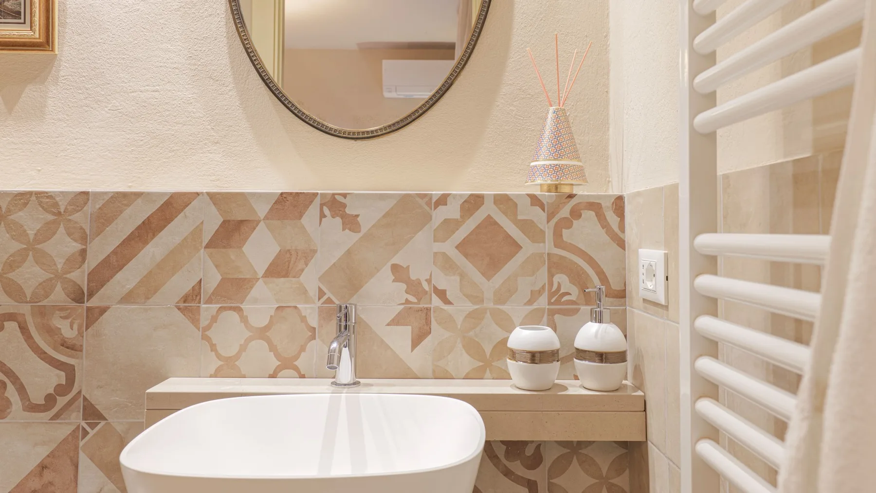 A bathroom vanity with a sink, patterned tile, and a round mirror.